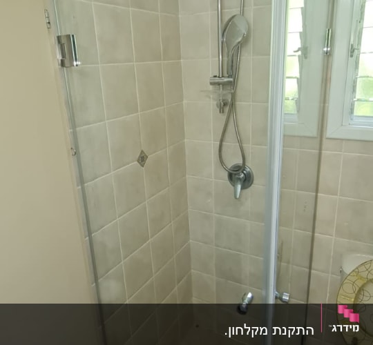 מקלחון זכוכית עם ראש מקלחת מתכת על קיר אריחים